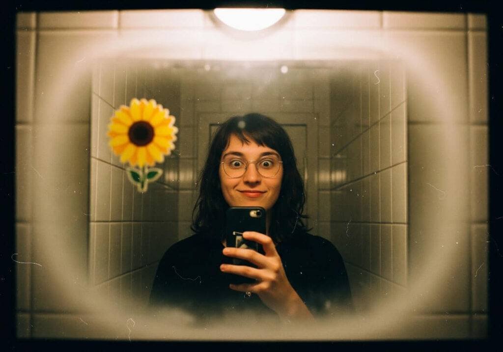 A grainy selfie of a person in a cramped bathroom mirror,